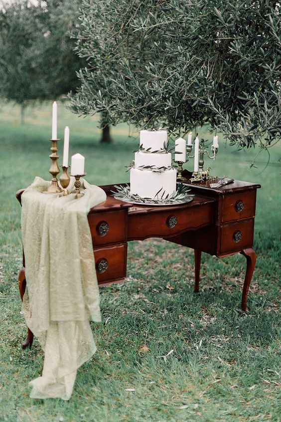 a dark-stained vintage dresser with green fabric and candles, a white wedding cake with olive greenery for a chic Italian wedding