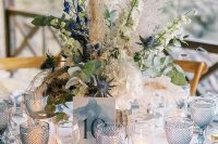 a delicate and elegant wedding tablescape with serenity blue chargers and glasses, a watercolor table number, white and blue bloom centerpiece