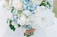 a delicate wedding bouquet featuring blue hydrangeas, light pink roses, lush white peonies is a beautiful idea for a summer wedding