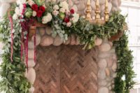 a fireplace clad with tiles and stone, with candles inside and a lush greenery and bloom garland on top