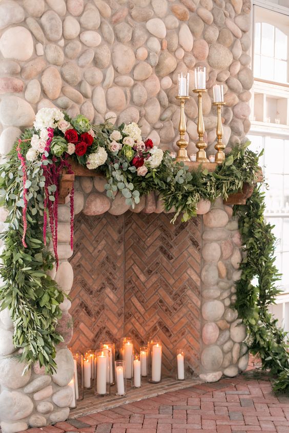 a fireplace clad with tiles and stone, with candles inside and a lush greenery and bloom garland on top