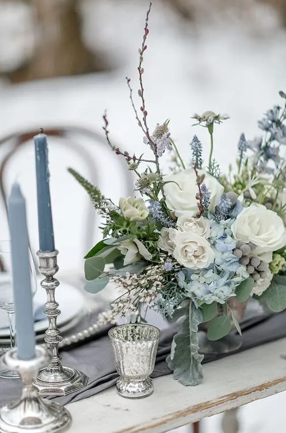 a grey and serenity blue winter wedding tablescape with a floral arrangement, mercury glass candleholders is very refined and chic