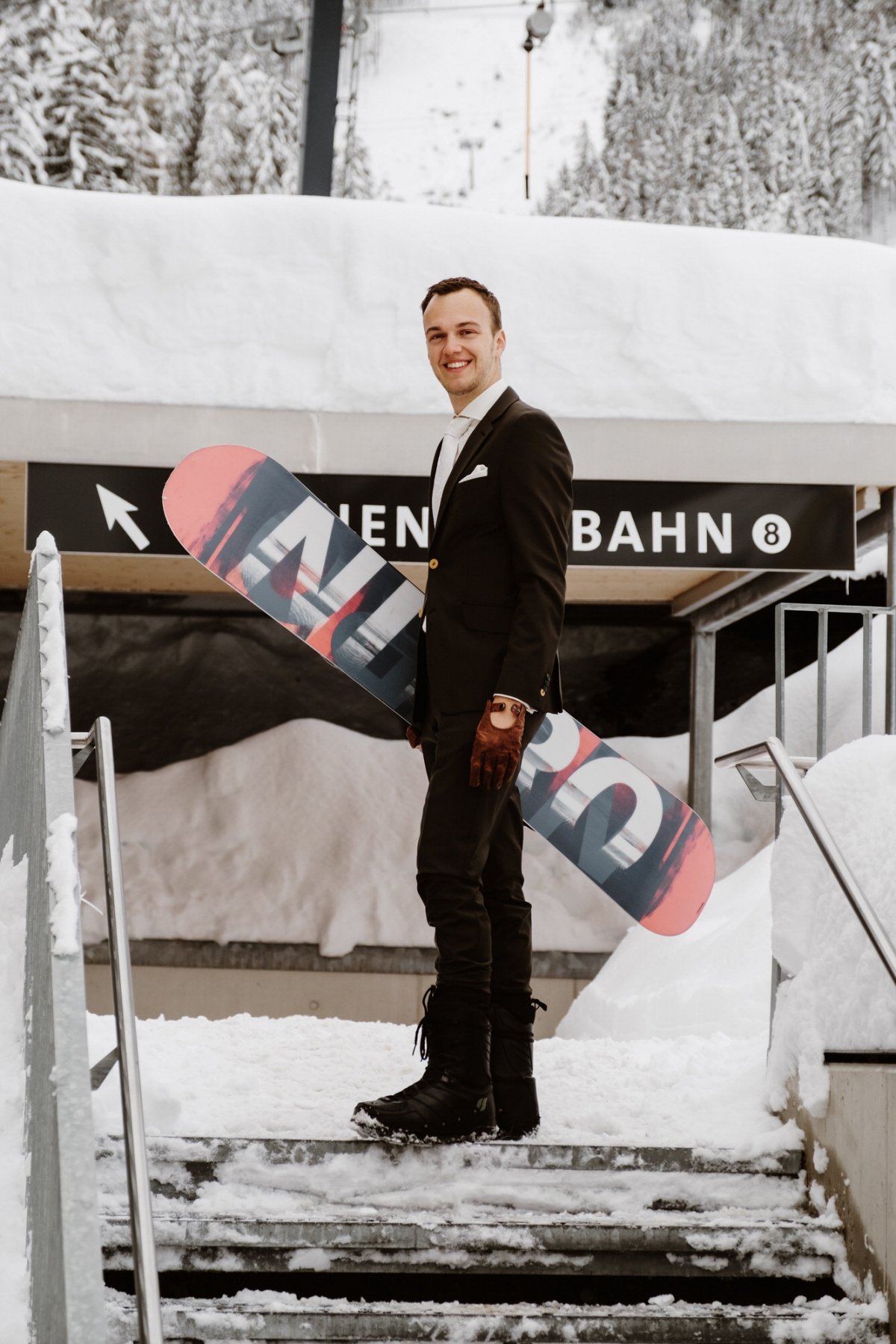A groom in snowboarding boots, gloves and his own snowboard for a cool and inspiring wedding portrait