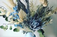 a lovely wedding centerpiece of a blue jar, dried blooms of natural colors and spray painted blue ones is amazing