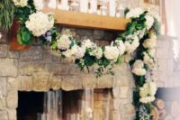 a lush hydrangea and greenery garland, pillar candles and floating candles in glasses make the rough stone fireplace cooler