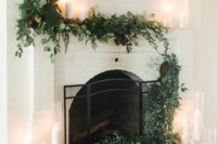 a lush textural greenery garland covering the mantel and fireplace and candles in tall glasses make it look modern and fresh
