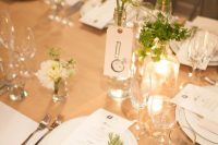 a modern neutral wedding tablescape with white linens, a kraft paper runner, a cluster centerpiece of greenery and white blooms plus candles