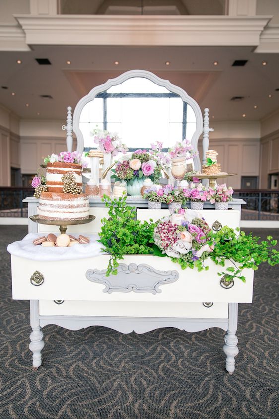 a neutral vintage dresser used as a dessert table, with pink blooms and greenery and some delicious wedding desserts to rock