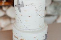a neutral wedding cake decorated with airplanes and topped with one for travel-lovers