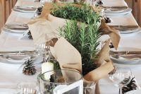 a neutral wedding reception tablescape with a kraft paper runner and potted plants wrapped with kraft paper, pinecones and white linens