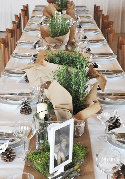 a neutral wedding reception tablescape with a kraft paper runner and potted plants wrapped with kraft paper, pinecones and white linens
