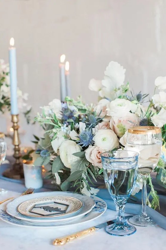a pastel wedding tablescape with a serenity blue table and glasses, blue candles, pastel and white blooms and blue thistles