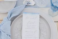 a powder blue table runner, napkin, an ombre menu, pebbles and seashells for a chic coastal look