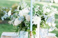 a pretty and chic wedding table setting with a serenity blue table runner, glasses, a blue and white centerpiece and glass plates