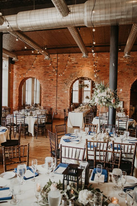 a pretty industrial wedding venue with brick walls, exposed pipes, blush and white blooms, navy and white linens