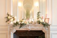 a refined vintage fireplace with lush florals, greenery and candles plus a large mirror