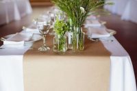 a relaxed neutral wedding tablescape with white linens, a kraft paper table runner, greenery and bloom arrangements for a laid-back wedding