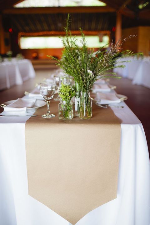 a relaxed neutral wedding tablescape with white linens, a kraft paper table runner, greenery and bloom arrangements for a laid back wedding
