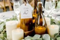 a romantic wedding centerpiece of wine bottles as candle holders and table numbers, pillar candles, a eucalyptus wreath around