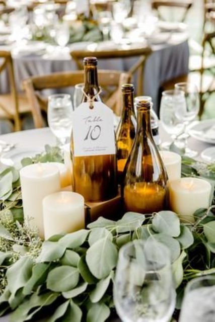 a romantic wedding centerpiece of wine bottles as candle holders and table numbers, pillar candles, a eucalyptus wreath around