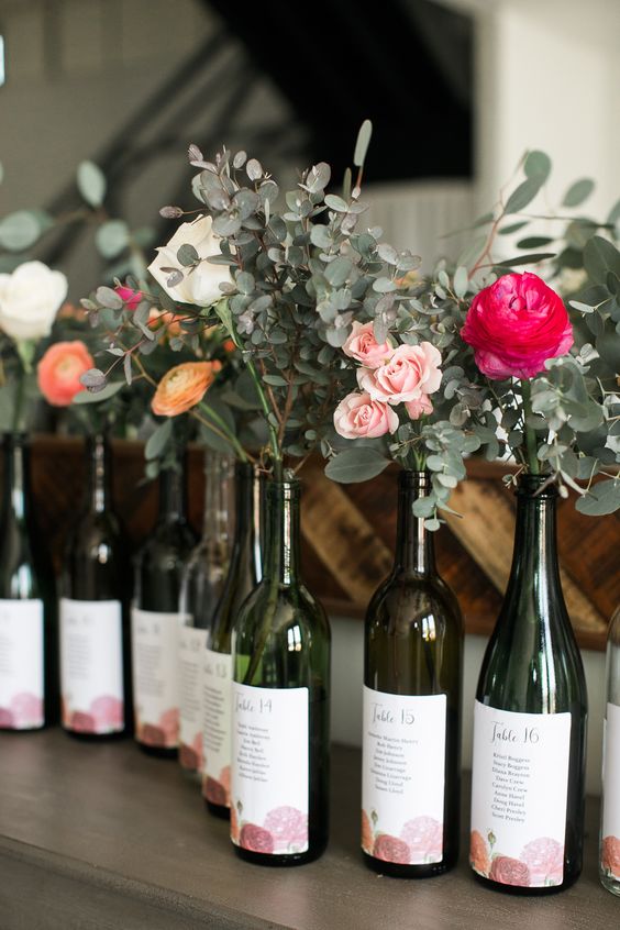a seating chart made of wine bottles, with fresh greenery and bright blooms is a pretty idea for a vineyard or just rustic wedding