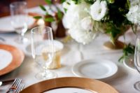 a simple and elegant wedding tablescape with terracotta chargers, white blooms and greenery and candles