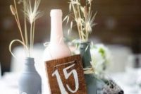 a simple and relaxed wedding centerpiece of beer and a wine bottle, dried grasses and a burlap table number is cool