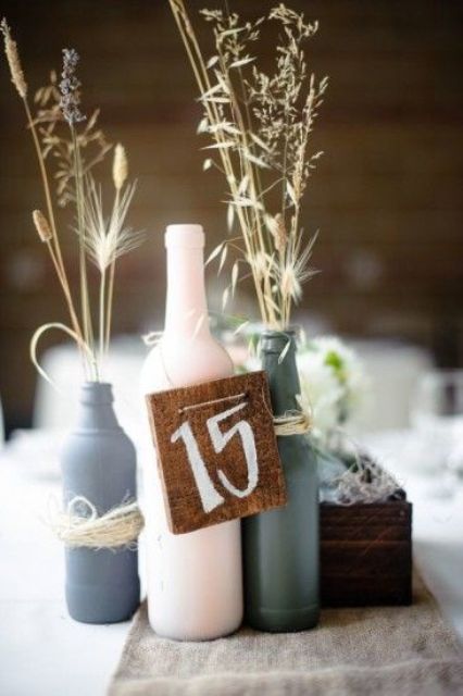 a simple and relaxed wedding centerpiece of beer and a wine bottle, dried grasses and a burlap table number is cool