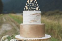 a ski resort or mountain wedding cake with a naked tier and a gold one and with a laser cut topper