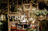 a sophisticated stained dresser decorated with greenery, potted greenery, a cage, a wedding cake and some empty frames in the back
