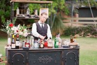 a vintage black dresser used as a wedding bar, with blooms and greenery and an additional shelf in the backdrop