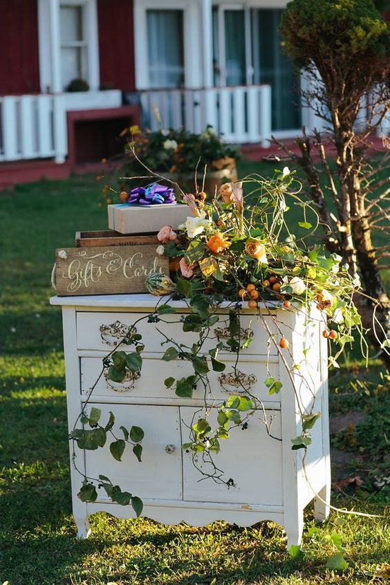 a vintage dresser with lovely wedding decor - a floral and greenery arrangement with fruit, wooden boxes with petals and a sign