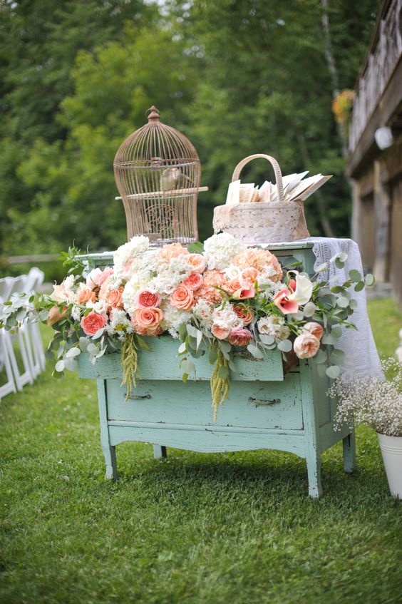 a vintage mint green dresser decorated with pastel and neutral blooms and greenery, with a cage on top and a basket with cards