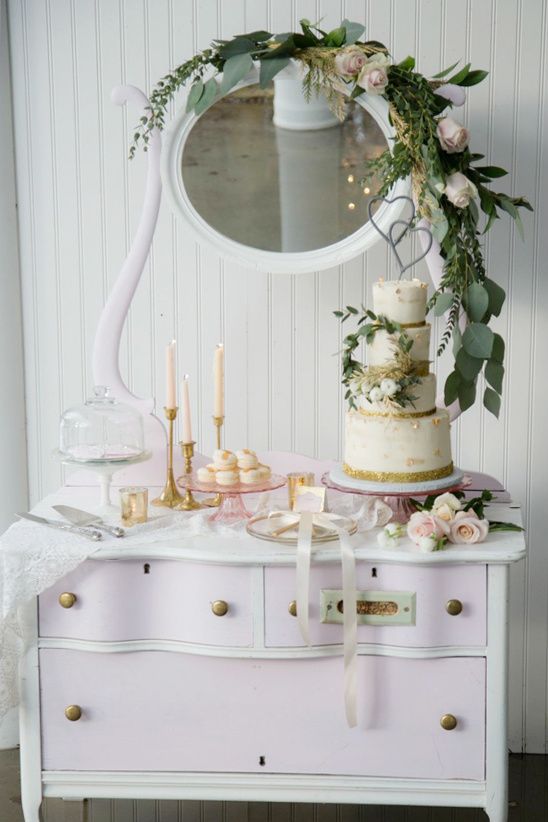 a vintage pink and white dresser with lace, greenery and pastel blooms, chic gold foil desserts and a wedding cake and pink candles
