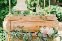 a vintage stained dresser with greenery and blooms, tall and thin candles, an ombre wedding cake with some wine is refined