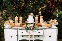 a vintage white buffet with a floral arrangement and lots of delicious desserts, sweets and cakes is wow