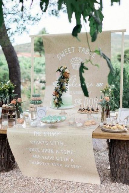 a wedding dessert table with a kraft paper backdrop with quotes, an ombre green wedding cake and lots of delicious sweets