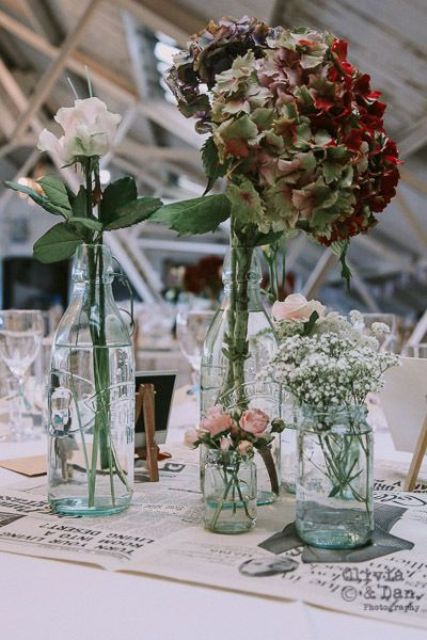 a wedding reception table decorated with newspapers , with bottles with various fresh blooms is a gorgeous idea