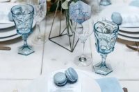 a white and serenity blue winter wedding tablescape with blue napkins, glasses and macarons plus gold cutlery is chic