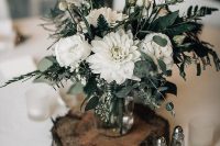 a white floral centerpiece with greenery and candles around placed on a wooden slice is a good decor idea for a ski resort wedding