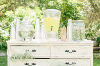 a white vintage dresser decorated with baby’s breath and with lemonade and water tanks as a wedding drink station