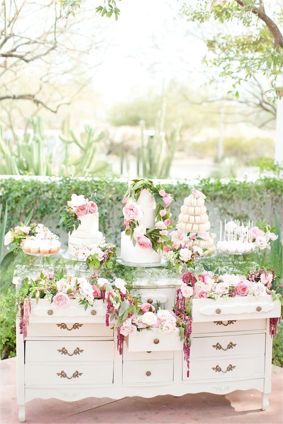 a white vintage dresser decorated with blush and mauve blooms, greenery and with lots of desserts, sweets and wedding cakes is wow