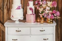a white vintage dresser with pink and neutral blooms in a gold vase, gold candleholders, white and pink cakes with pink blooms