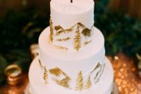 a white wedding cake with gold fir trees and mountains, a calligraphy topper is a chic idea for a ski resort wedding