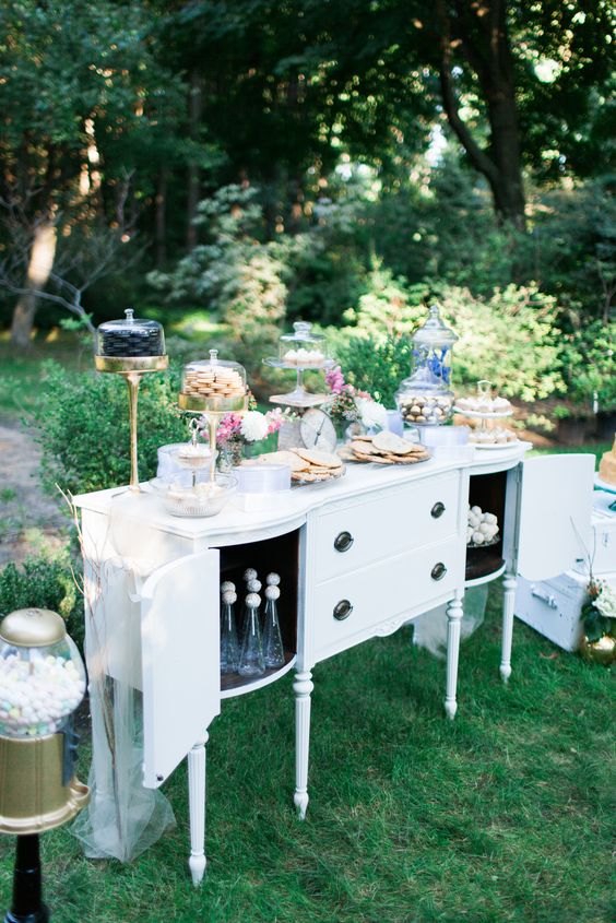 an antique white buffet as a wedding dessert table, with sweets, candies and cookies on the buffet and inside it