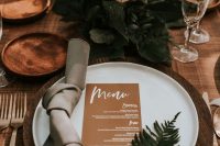 an elegant and chic wedding tablescape with wooden chargers, white plates, delicate blush and rust blooms, a kraft menu and greenery