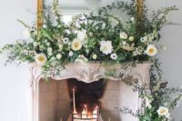 an exquisite fireplace with candles inside it, a vintage framed mirror and lush greenery and white blooms