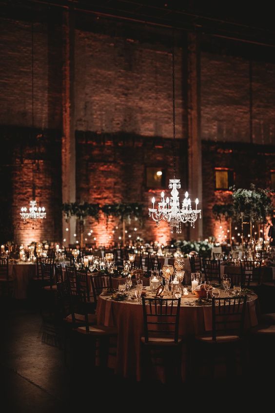 an industrial venue with brick walls, chic chandeliers, tall greenery centerpieces and candles is a lovely idea