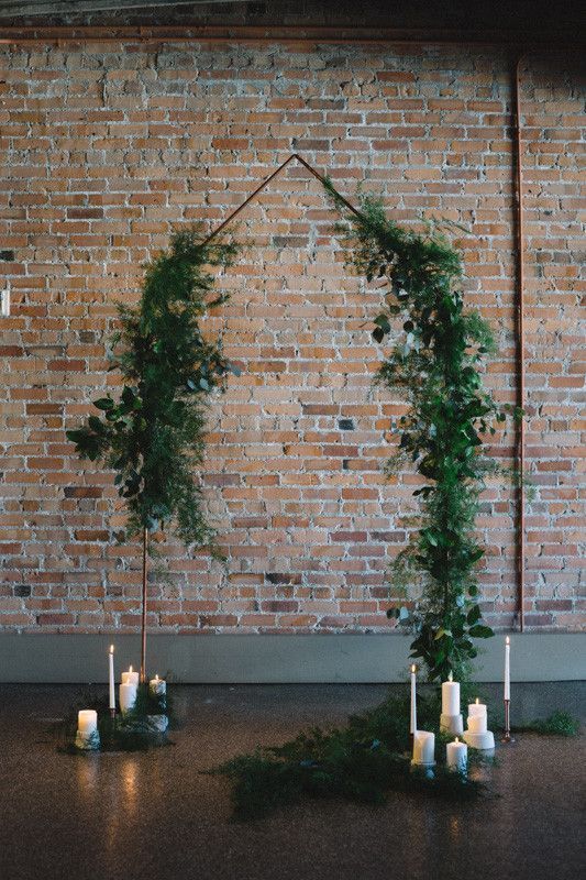 an industrial wedding ceremony space with a greenery wedding arch and pillar candles on the floor