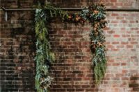 an industrial wedding ceremony space with greenery and dried foliage, pillar candles and a boho rug looks chic